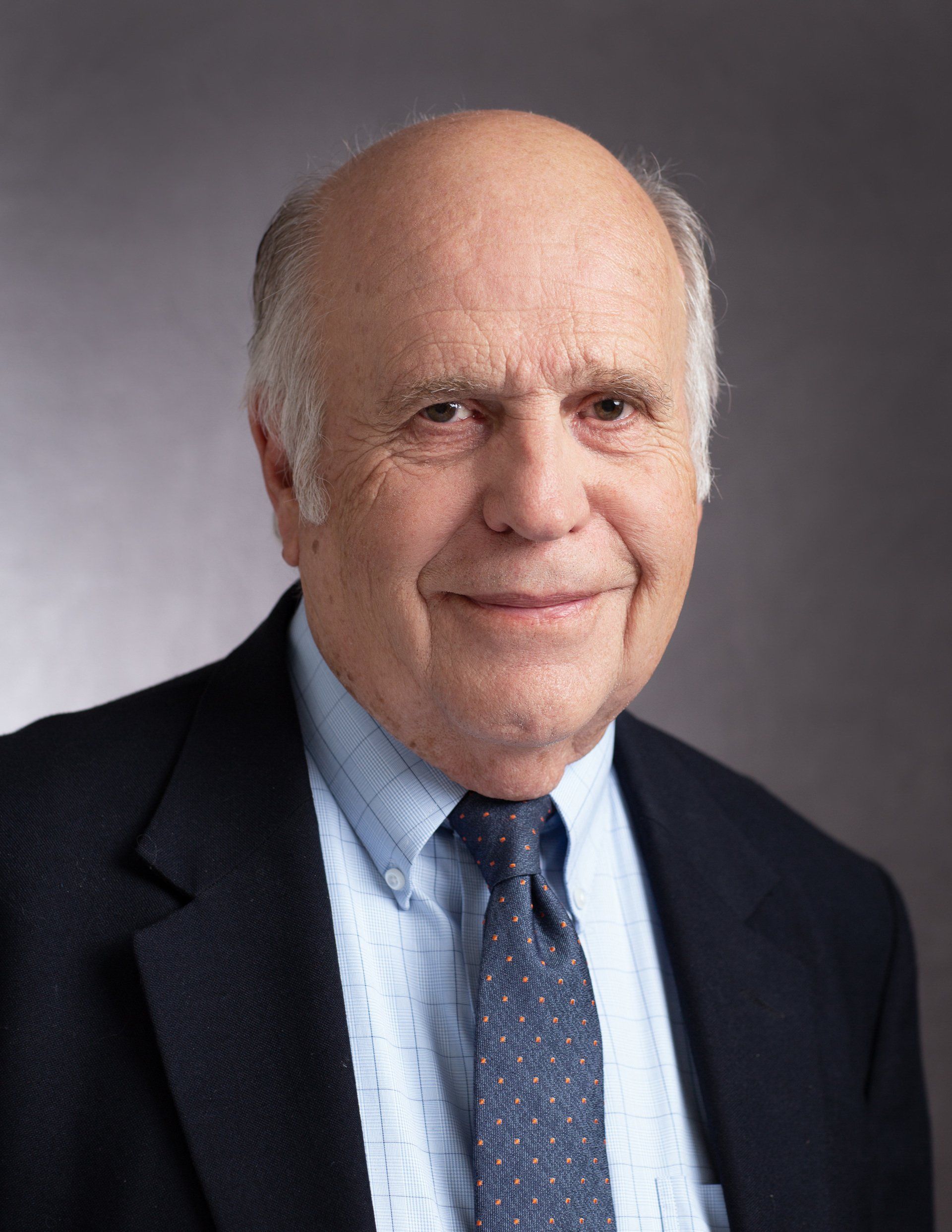 A bald man wearing a suit and tie is smiling for the camera.