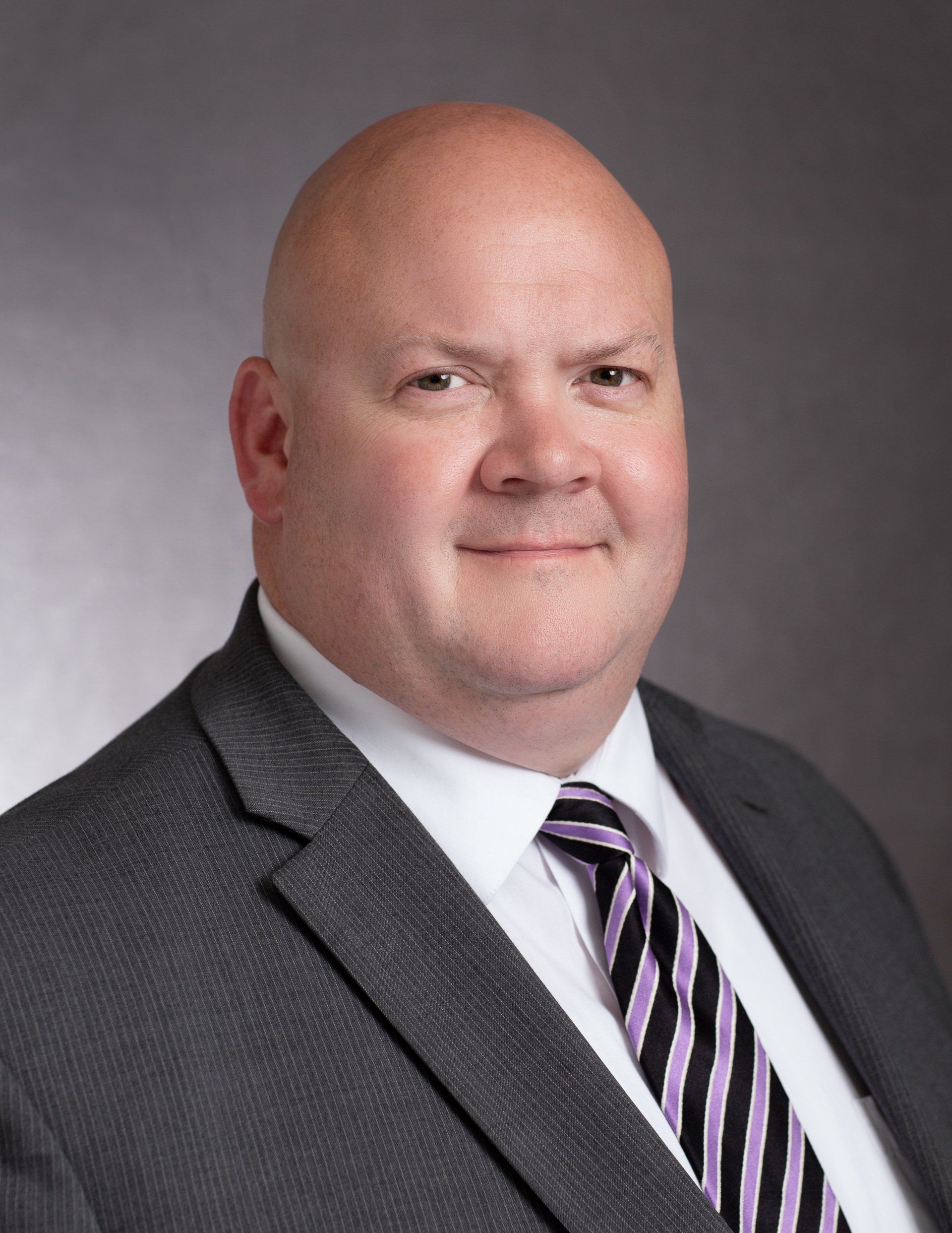 A bald man in a suit and tie is smiling for the camera.
