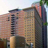 A tall building with a lot of windows is surrounded by other buildings.