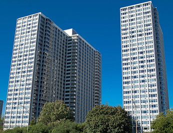 Two tall buildings against a blue sky with trees in the foreground