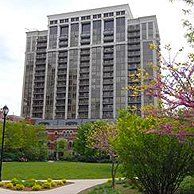A large building with a lot of windows is surrounded by trees and bushes in a park.