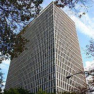 A tall building with a lot of windows is surrounded by trees and a street light.