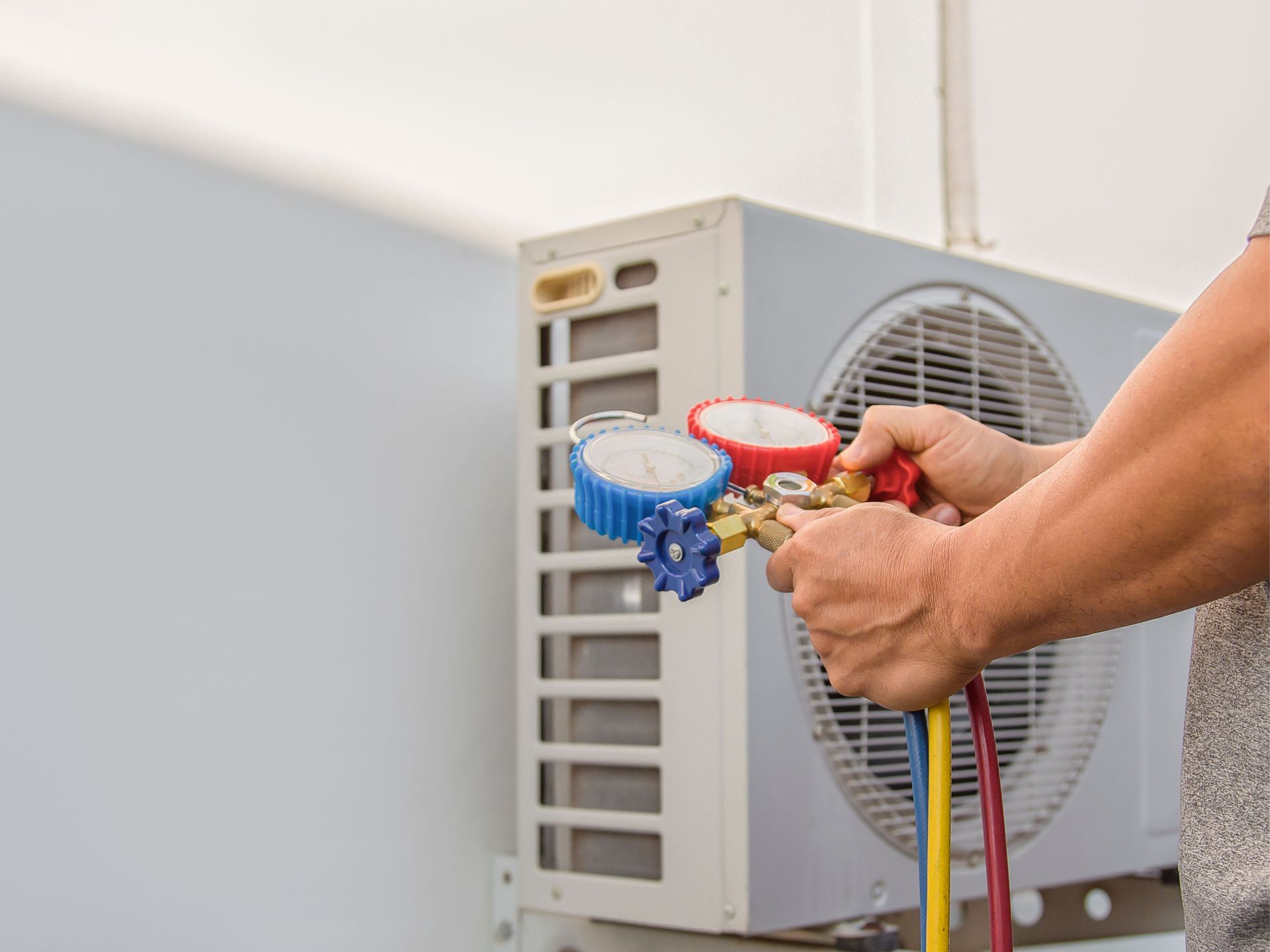 A man is using a gauge to check the pressure of an air conditioner.