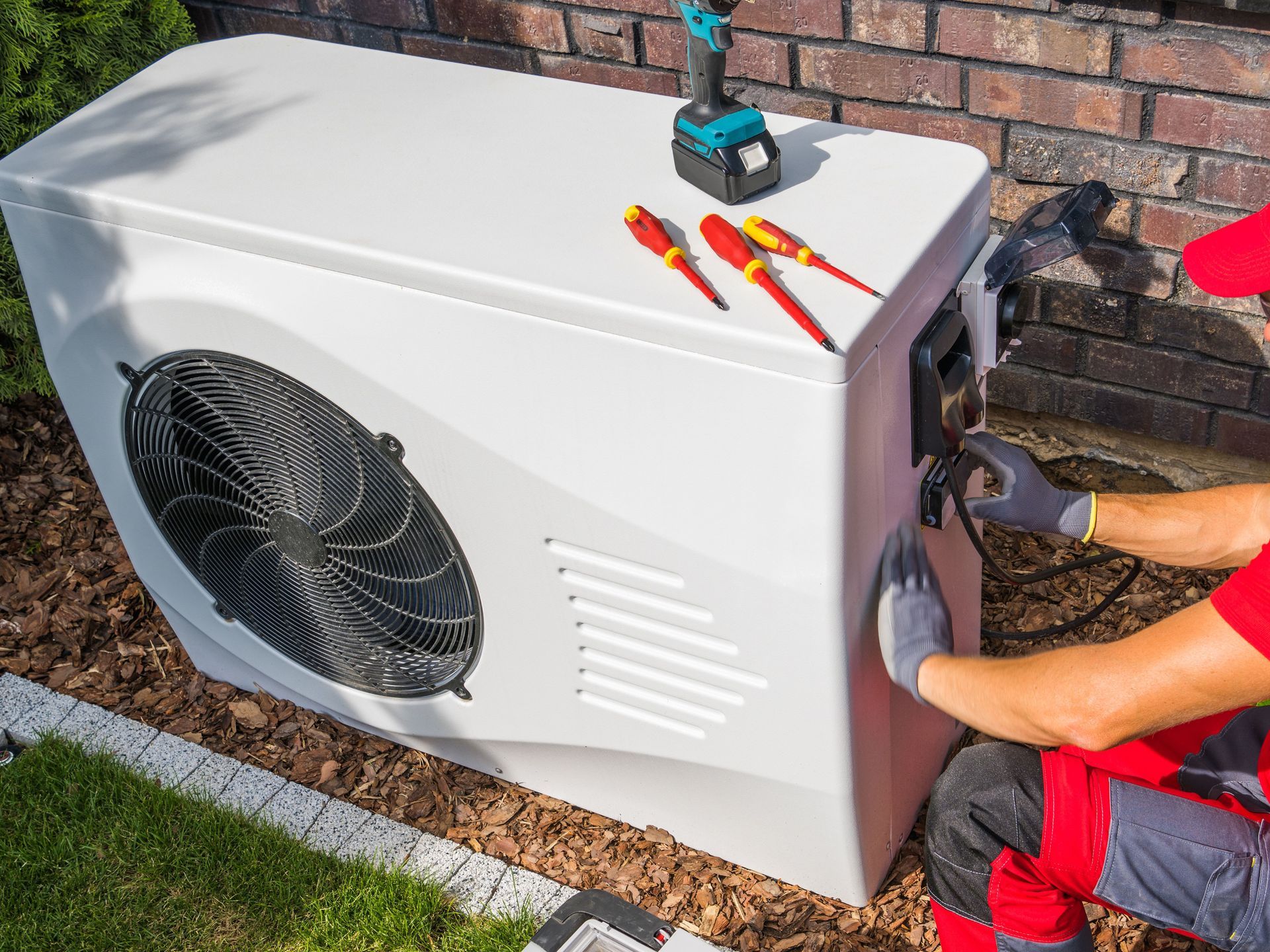 A man is working on an air conditioner outside of a house.