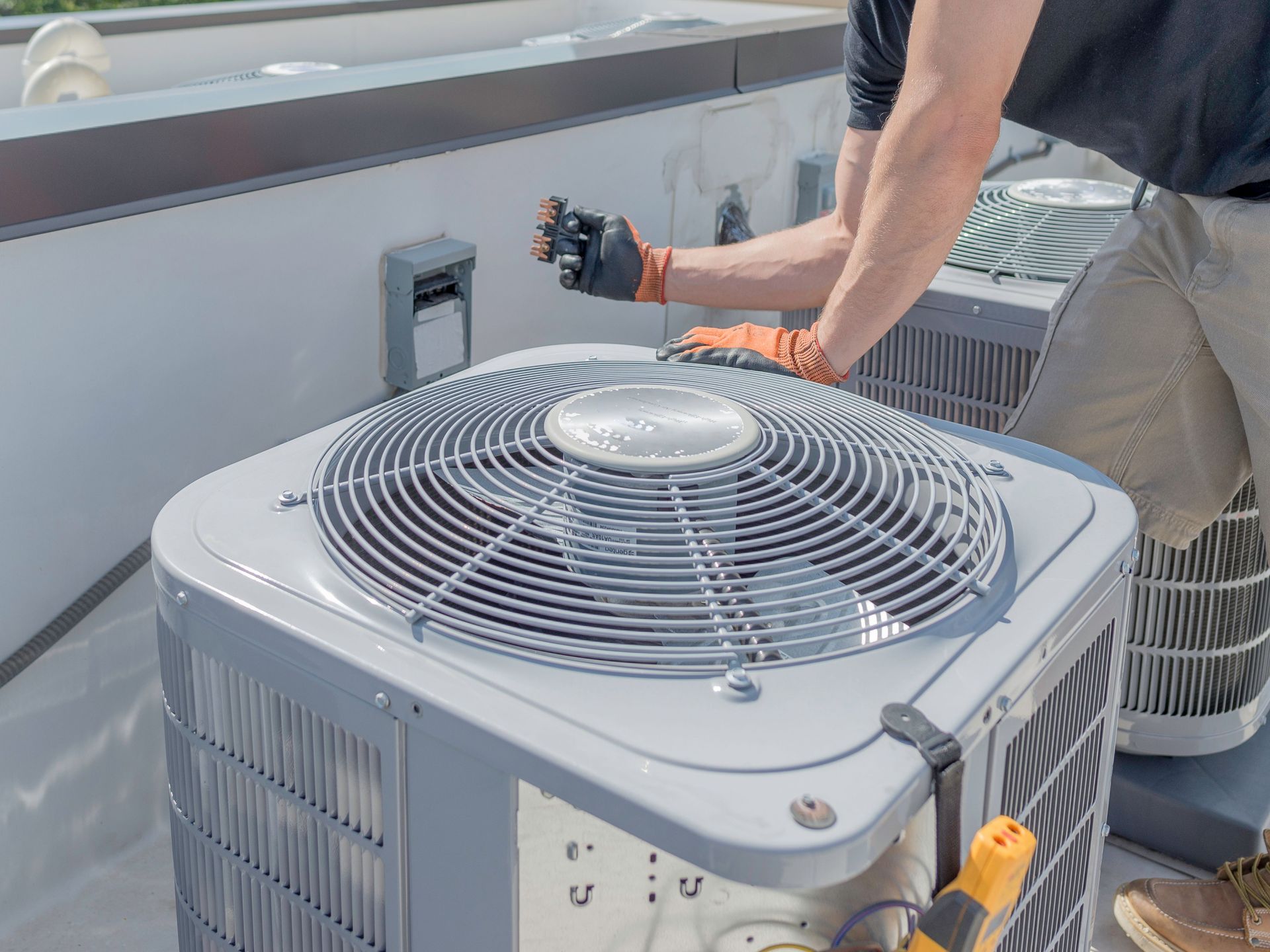 A man is working on an air conditioner on the roof of a building.