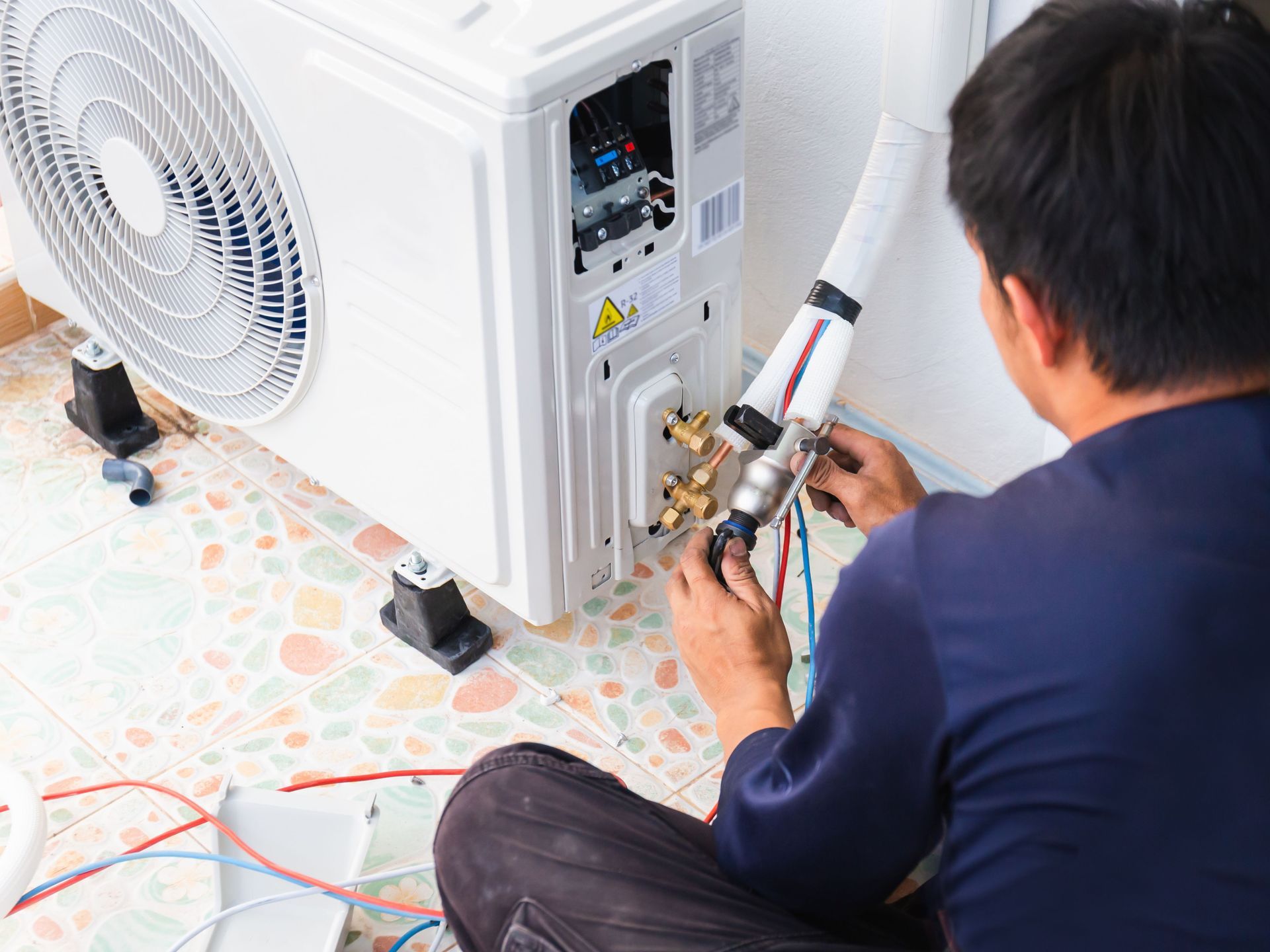 A man is sitting on the floor fixing an air conditioner.