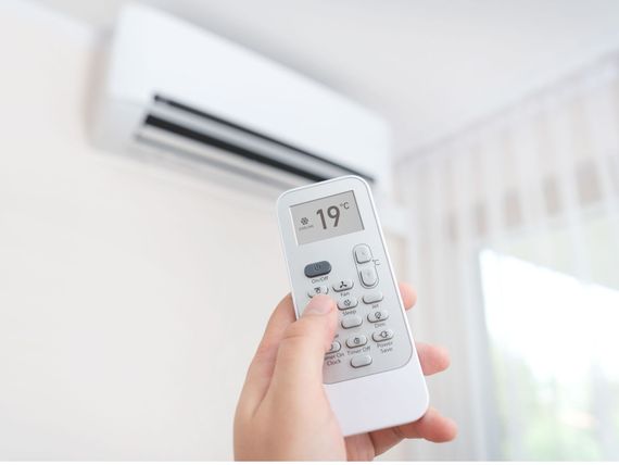 A person is holding a remote control in front of an air conditioner.