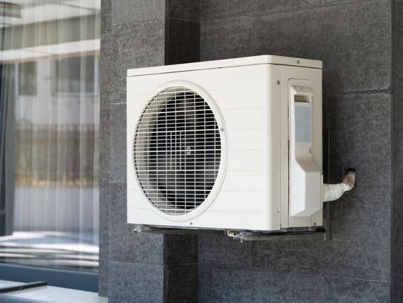 A white air conditioner is mounted on the side of a building.