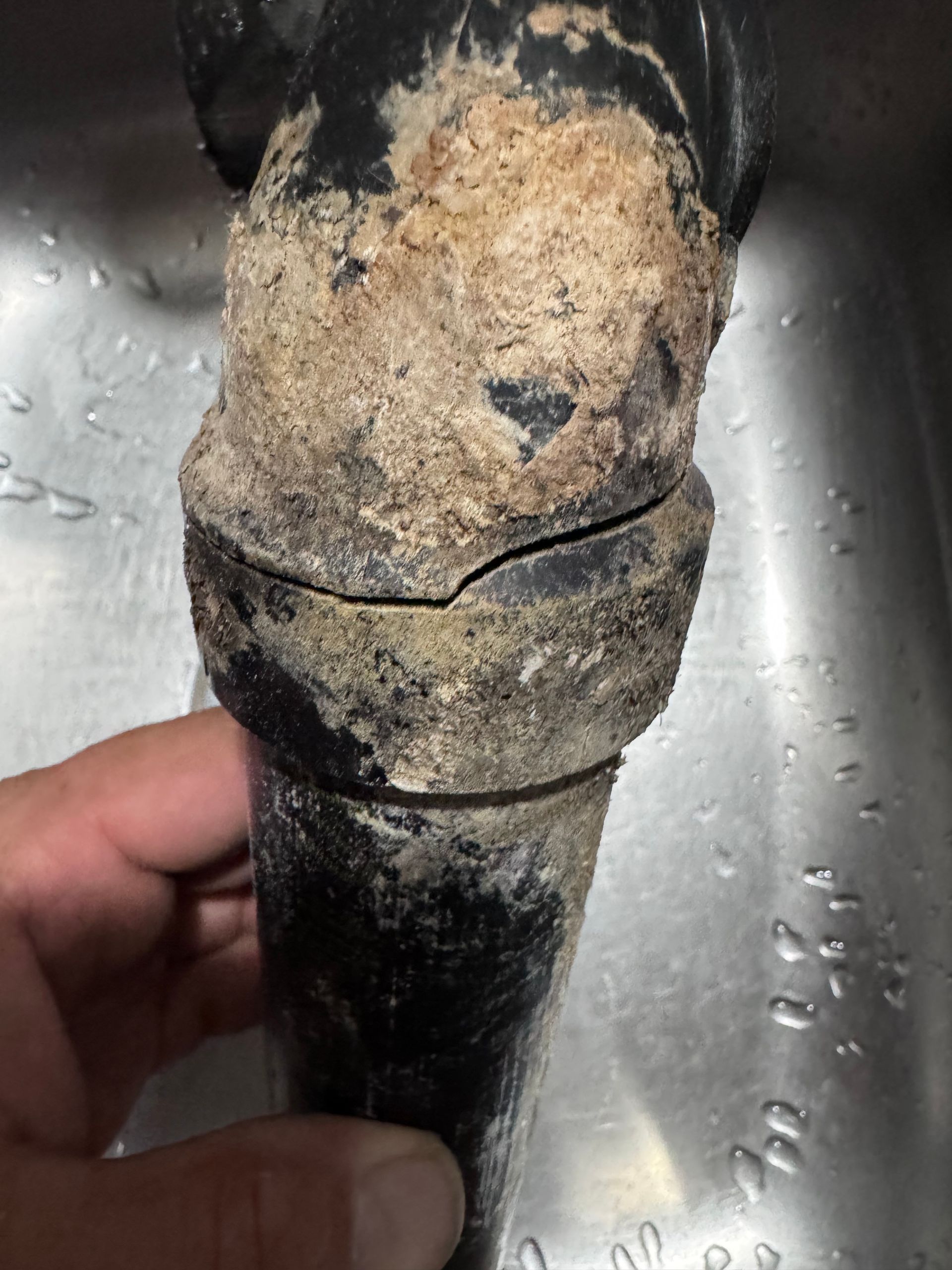 A person using a wrench to tighten bolts on a blue pipe clamp underground.