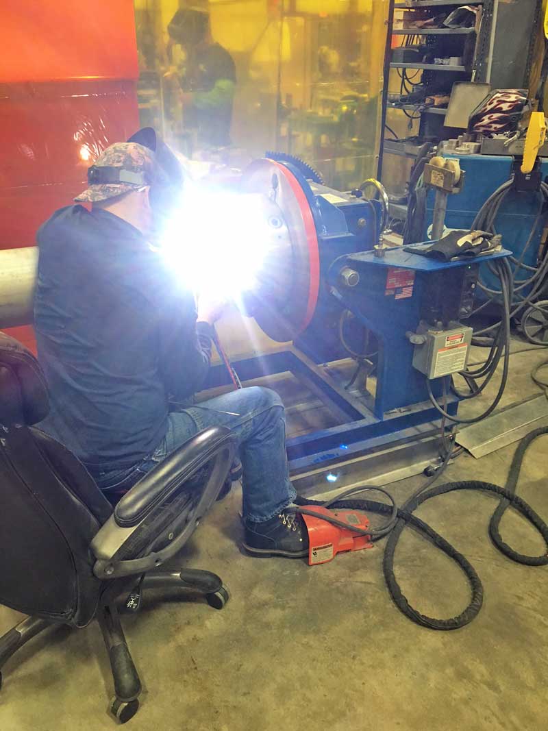 A man is sitting in a chair welding a piece of metal.