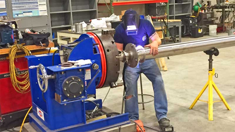 A man is welding a pipe in a factory.