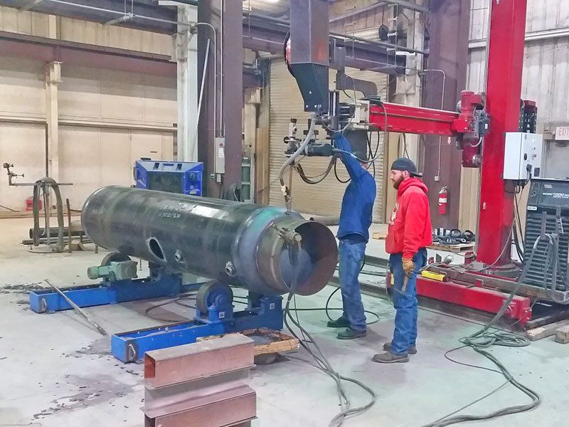 Two men are welding a large pipe in a factory.