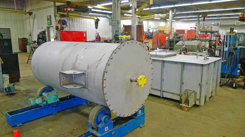 A large metal tank is sitting on top of a blue roller in a factory.