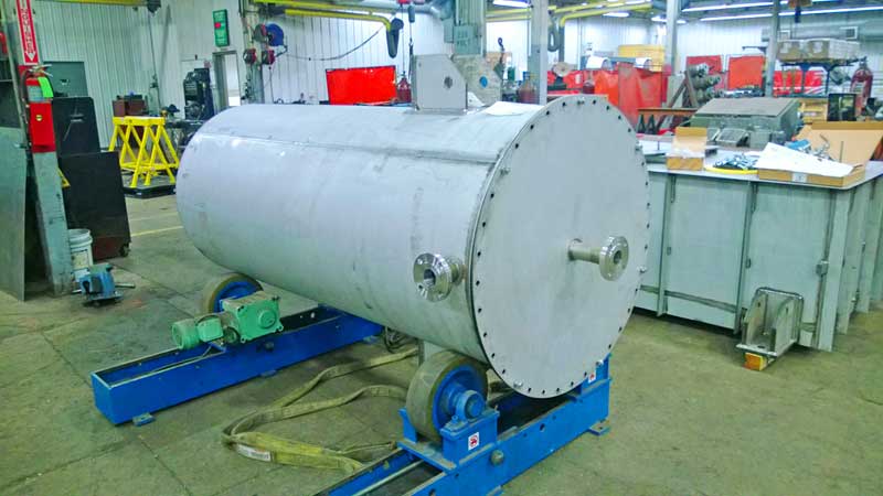 A large stainless steel tank is sitting on a conveyor belt in a factory.