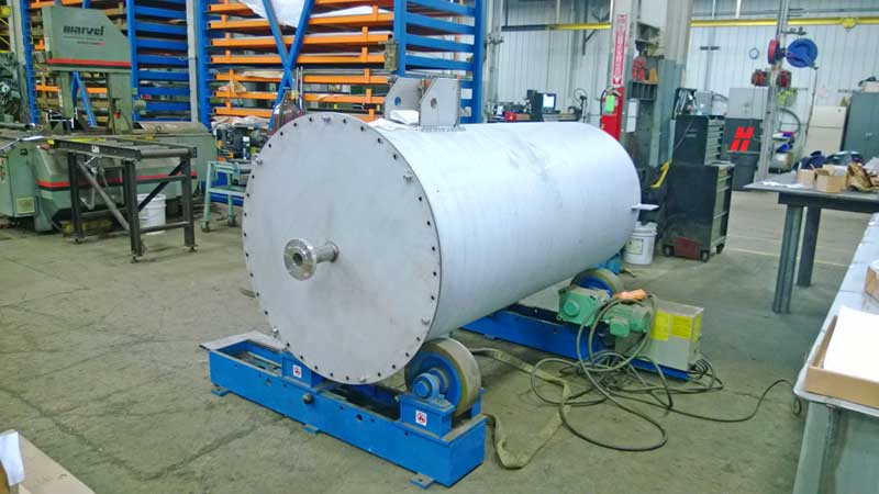 A large stainless steel tank is sitting on a machine in a factory.
