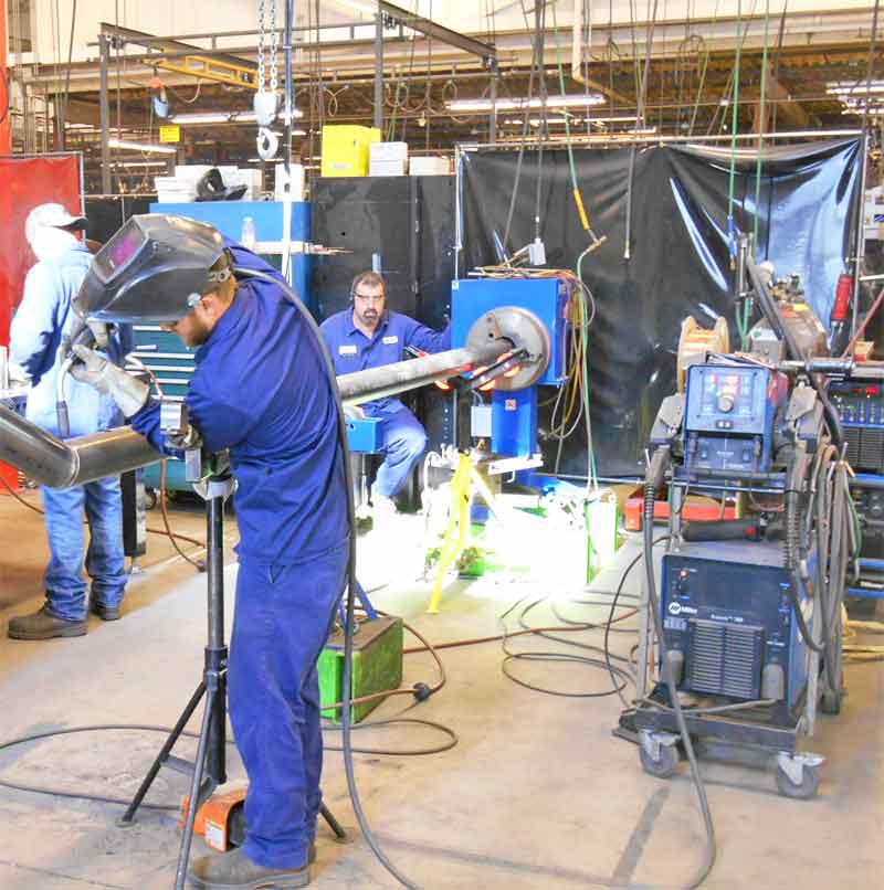 A man wearing a welding helmet is working on a pipe