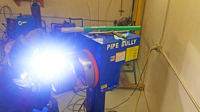 A man is welding a pipe in a workshop with a pipe bully machine.