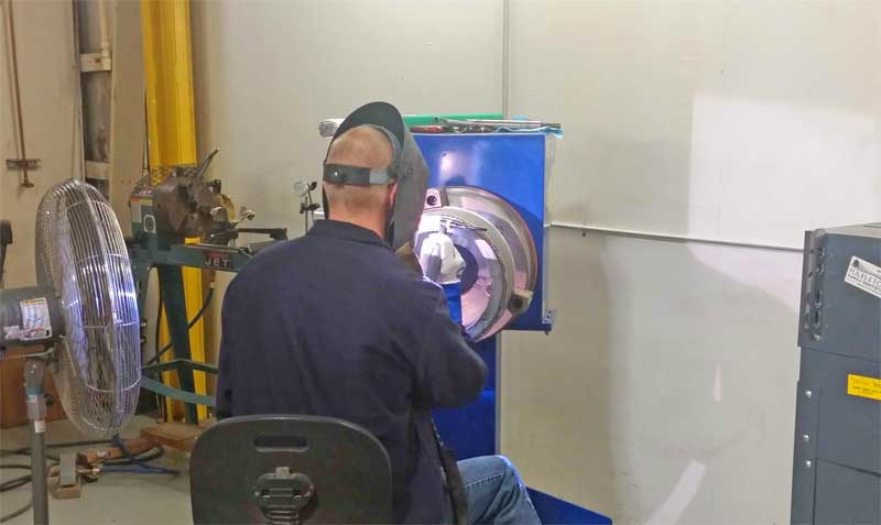A man wearing a welding mask is sitting in front of a machine.
