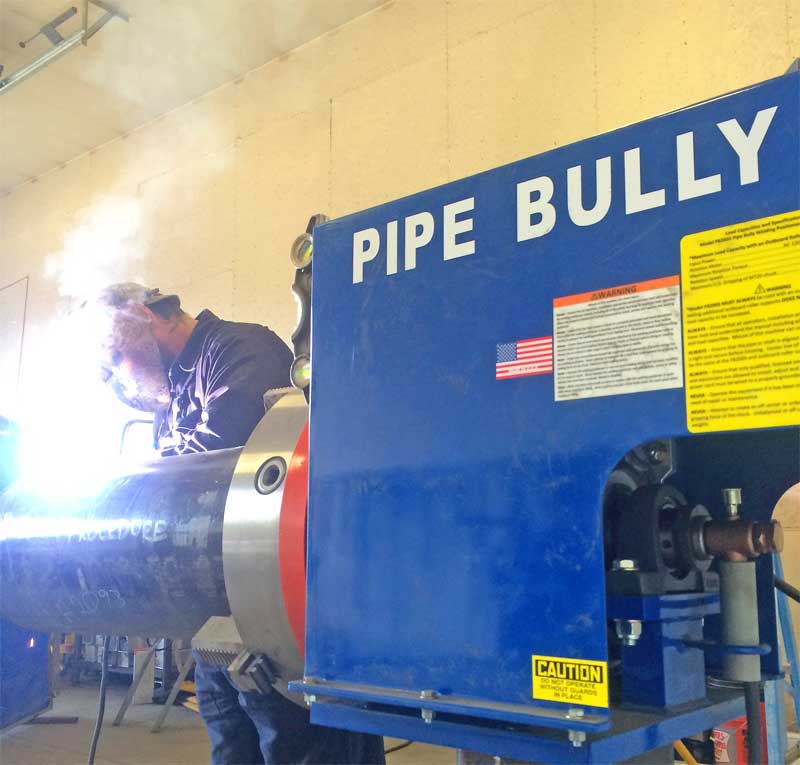 A man is welding a pipe next to a pipe bully machine