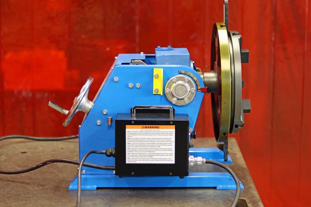 A blue machine is sitting on a table in front of a red curtain.