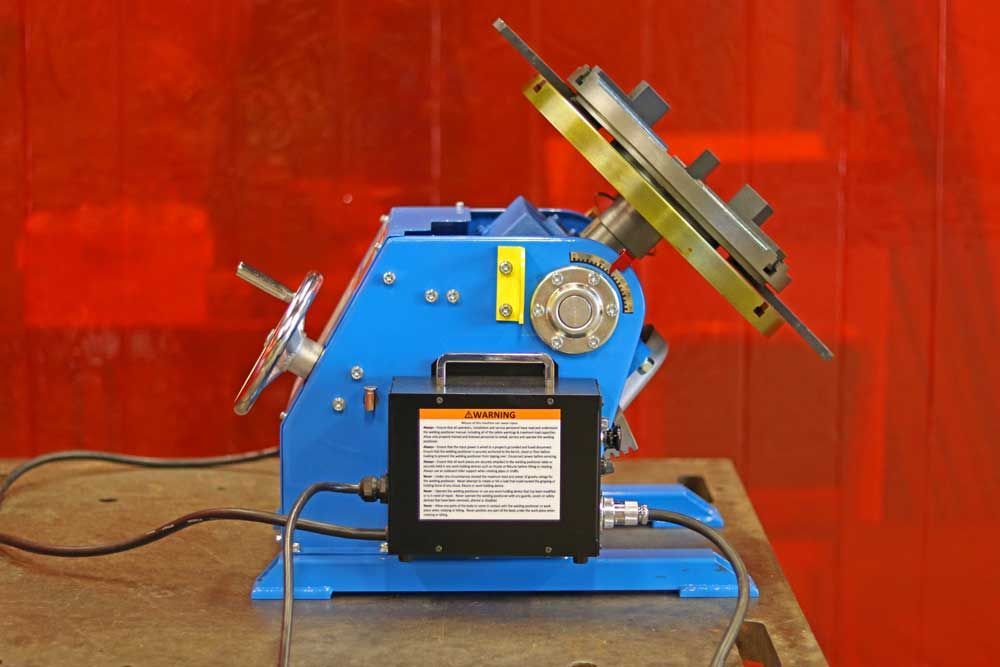 A blue machine is sitting on a table in front of a red curtain.