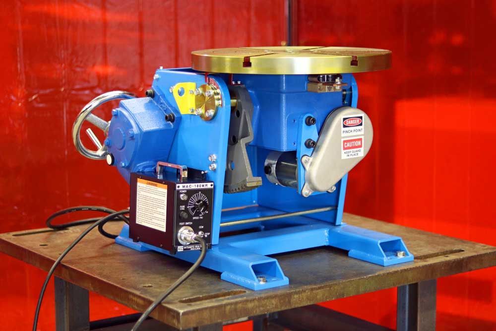 A blue welding machine is sitting on top of a wooden table.