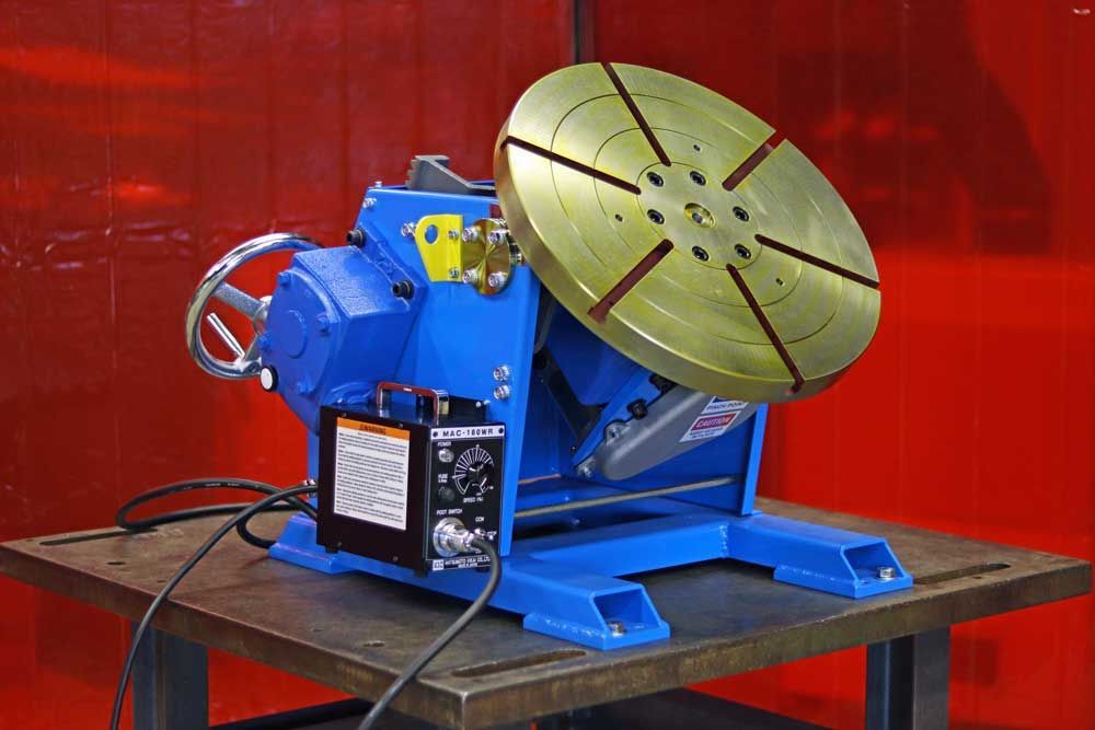A welding machine is sitting on a table in front of a red curtain.