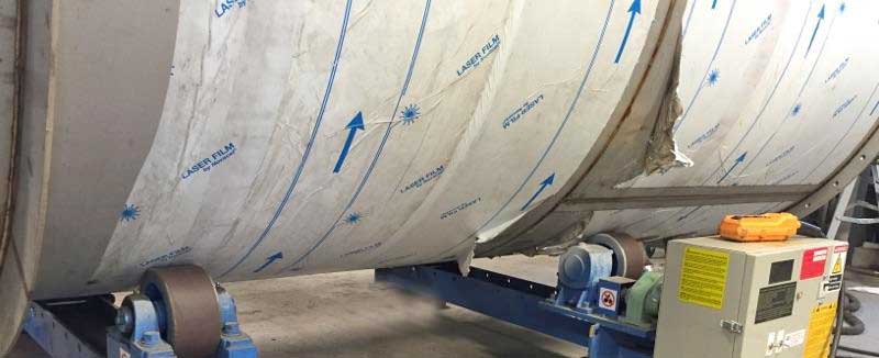 A large stainless steel tank is being rolled on a conveyor belt.