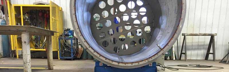 A large metal pipe with holes in it is sitting in a factory.