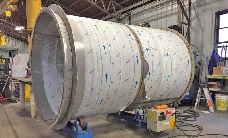 A large stainless steel pipe is being built in a factory.