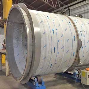 A large stainless steel pipe is sitting on a roller in a factory.