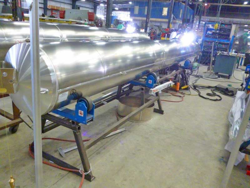 A large stainless steel pipe is being welded in a factory.