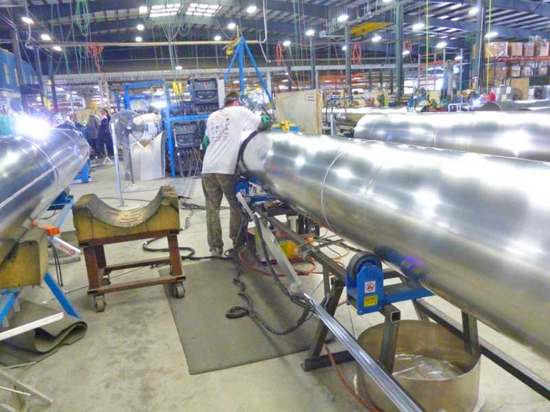 A man is welding a metal pipe in a factory.