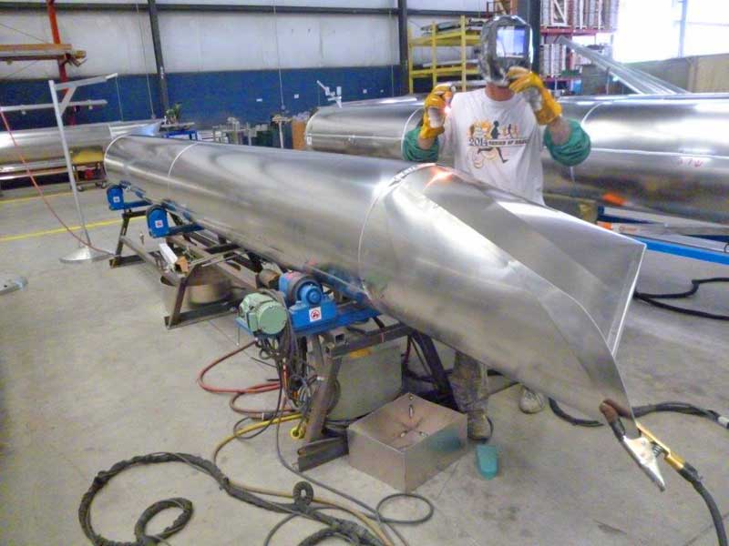A man is welding a large piece of metal in a factory