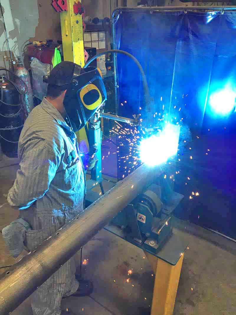 A man wearing a welding mask is welding a pipe