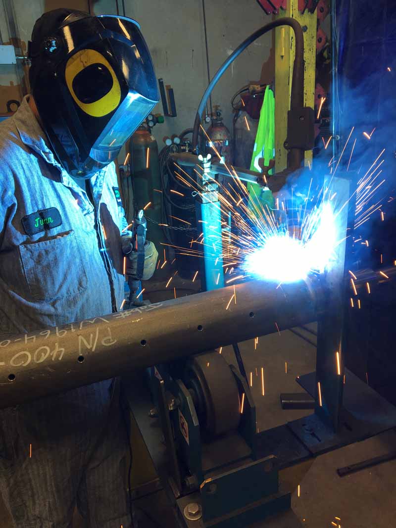 A man wearing a welding mask is welding a pipe