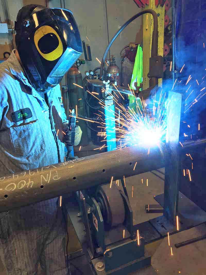 A man wearing a welding mask is welding a pipe