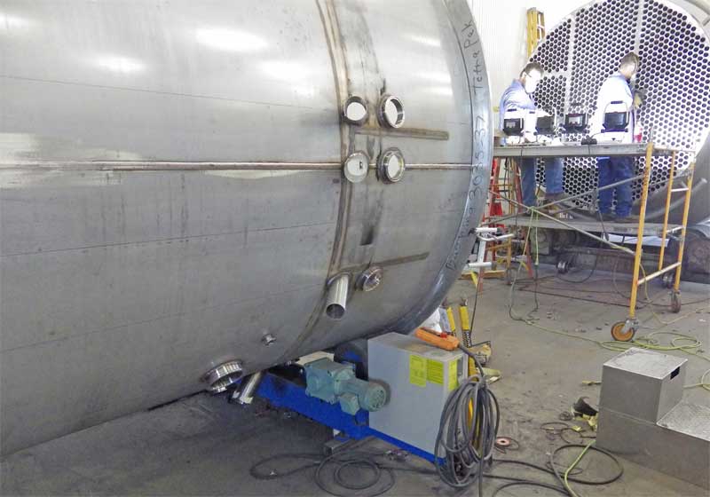 A large stainless steel tank is being built in a factory.