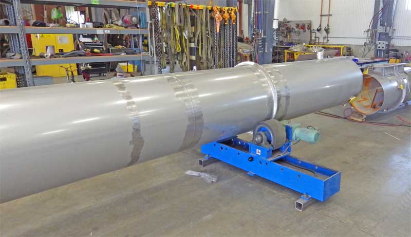 A large stainless steel pipe is sitting on top of a blue machine in a factory.