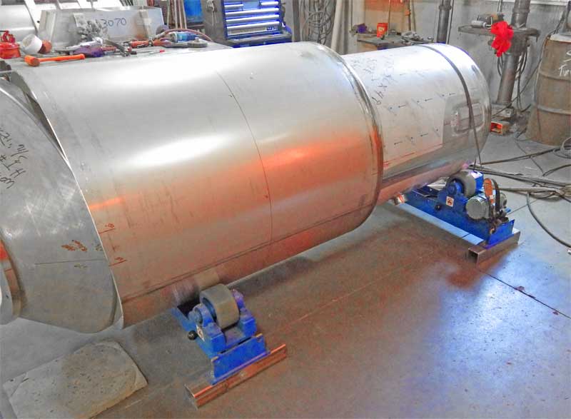 A large stainless steel tank is sitting on a table in a factory.