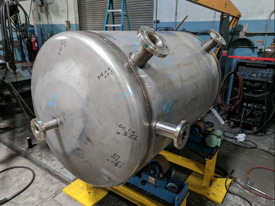 A large stainless steel tank is being built in a factory.