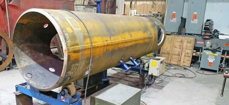 A large metal pipe is sitting on a machine in a factory.