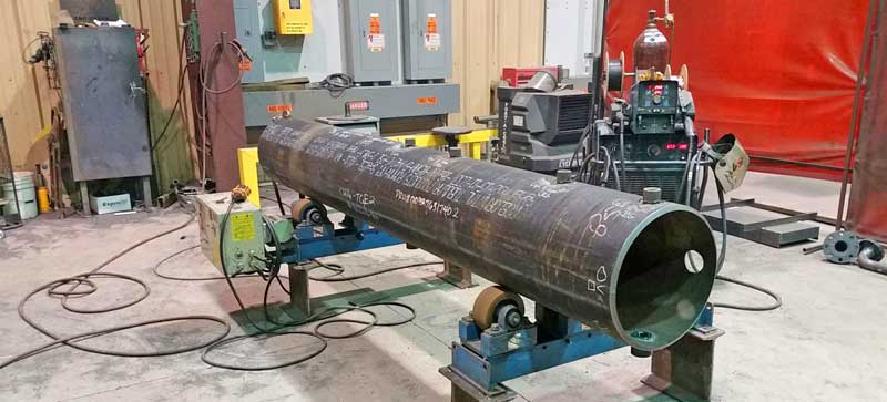 A large metal pipe is sitting on a machine in a factory.