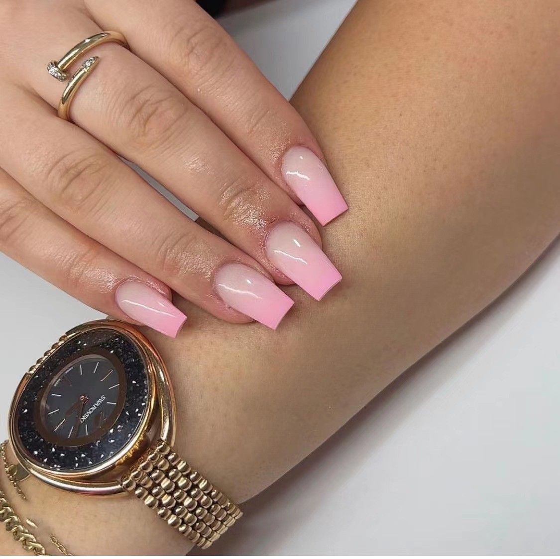 A woman wearing a watch and a ring has pink nails
