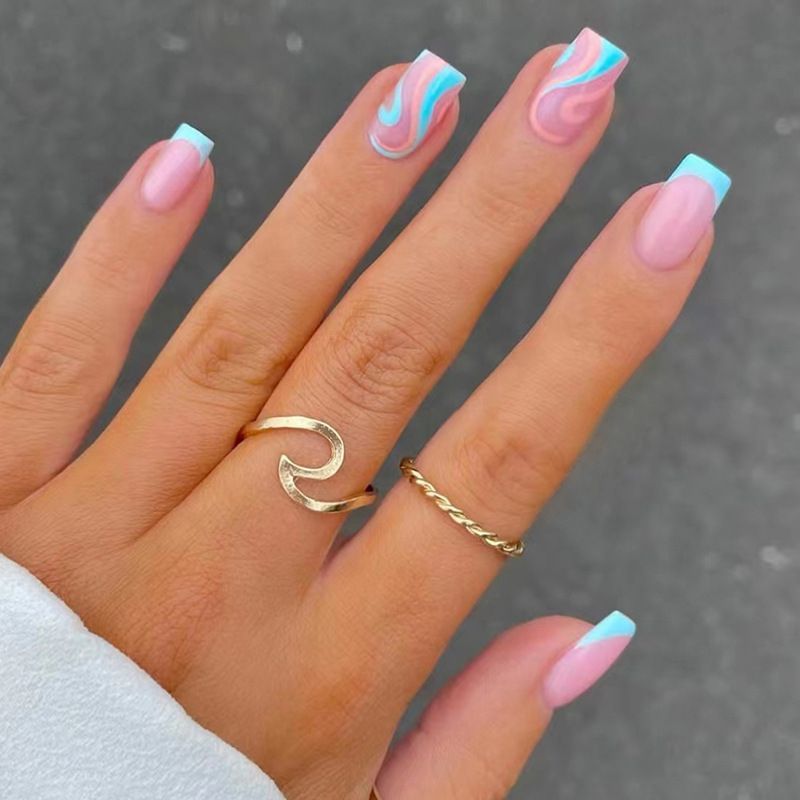 A woman 's hand with pink and blue nails and a wave ring
