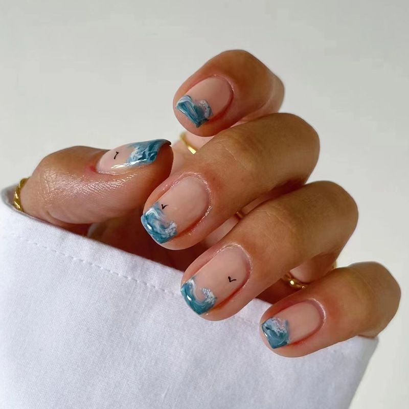 A close up of a woman 's nails with blue waves on them