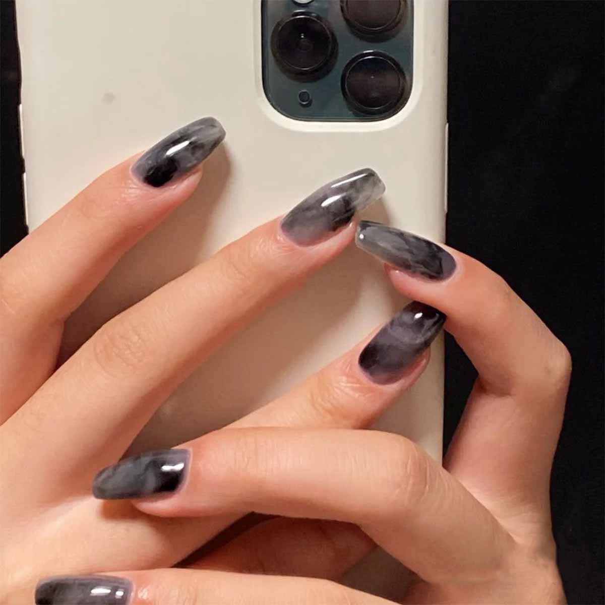 A woman with long black nails is holding a white phone