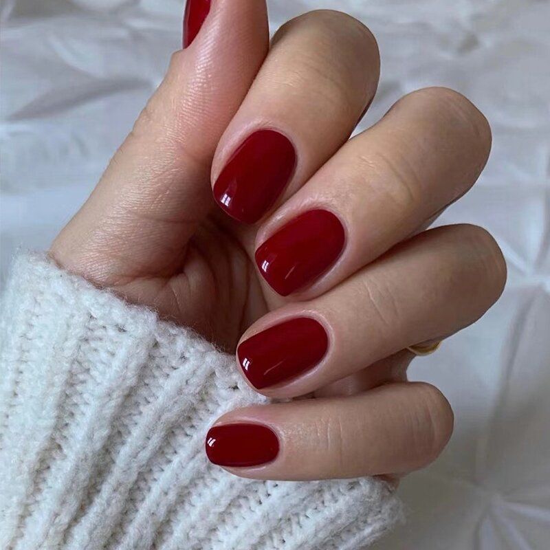 A woman wearing a white sweater has red nails