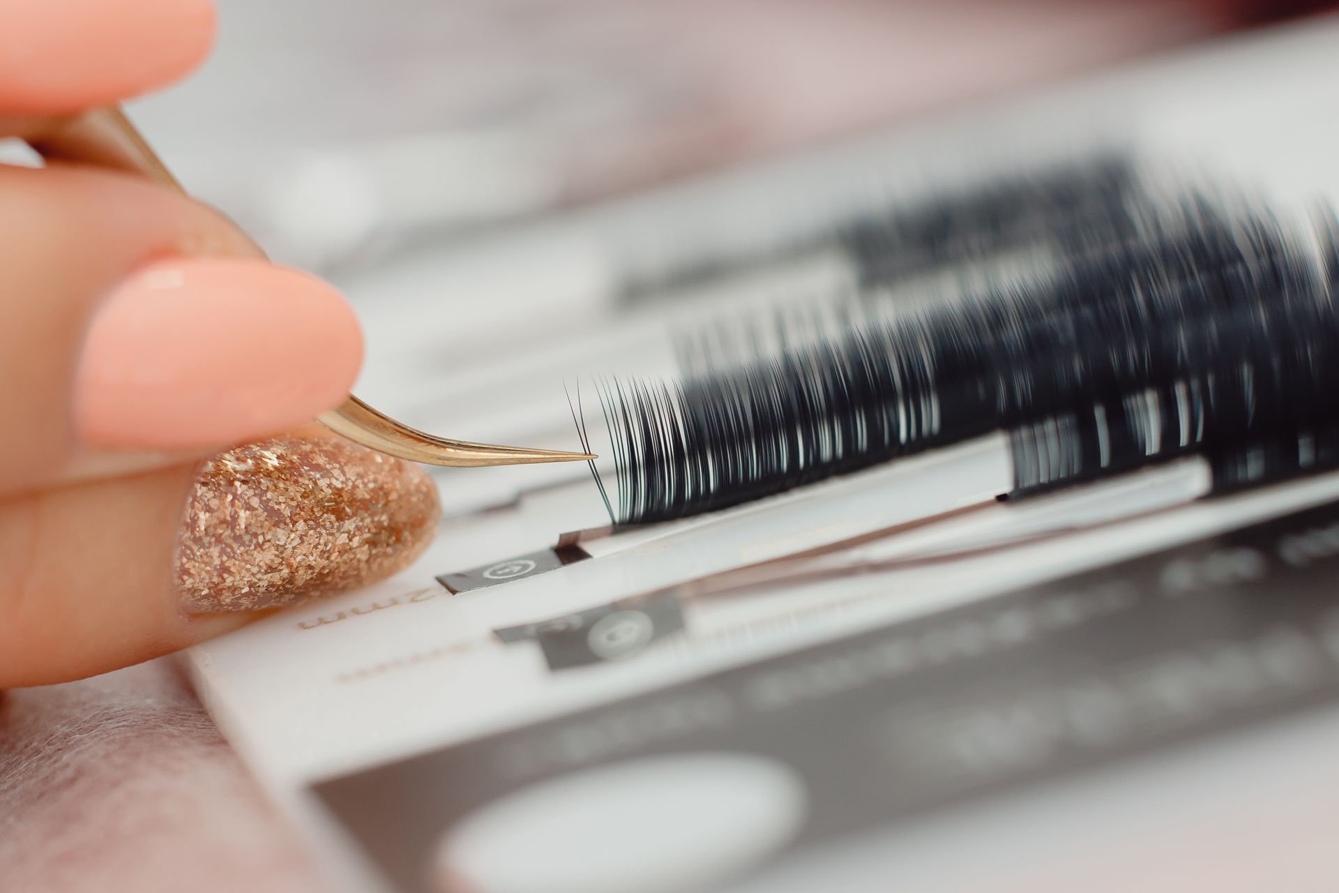 A close up of a person applying eyelashes with tweezers.