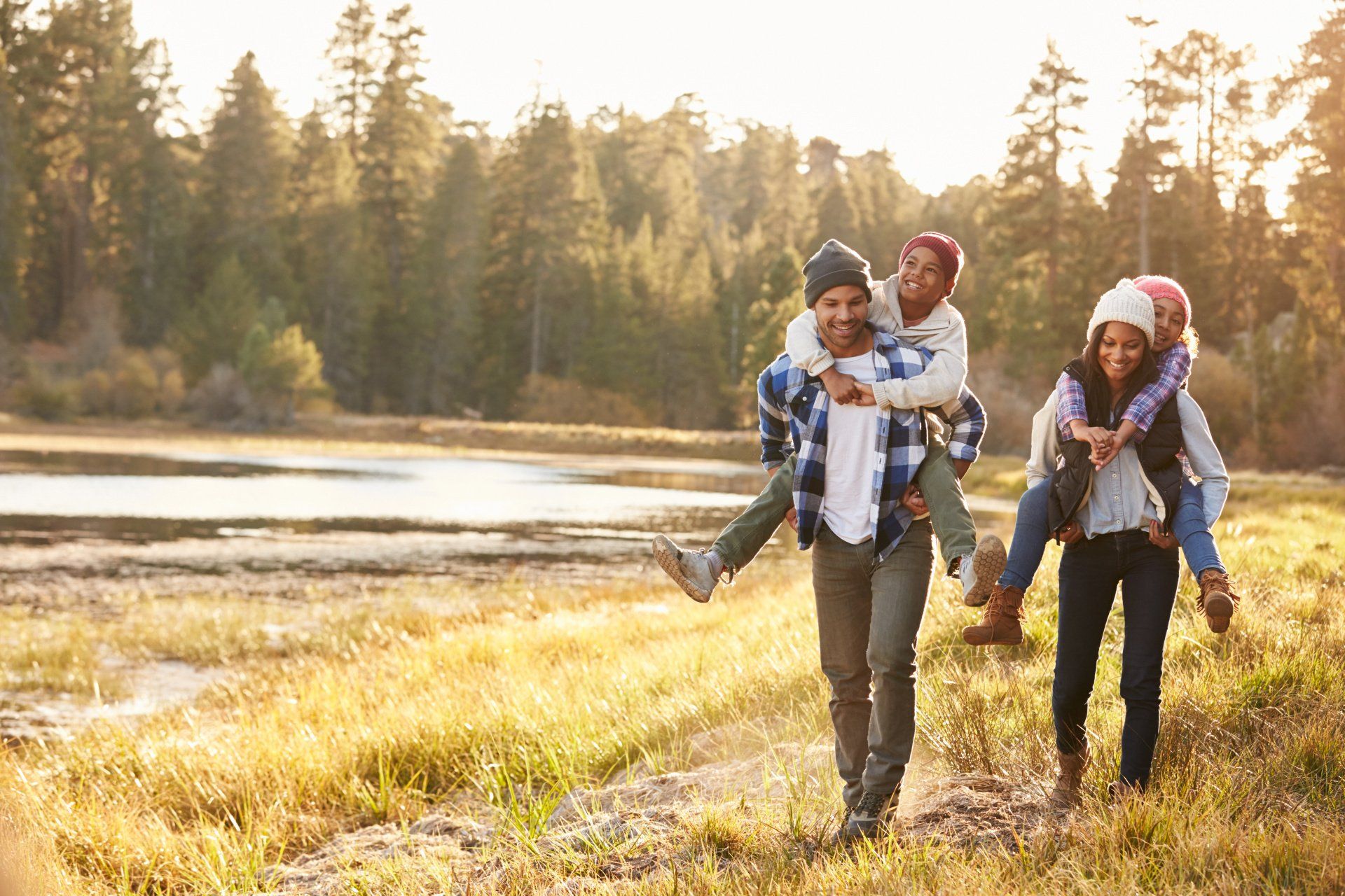 Family enjoys a sunny day by a lake: parents give children piggyback rides.